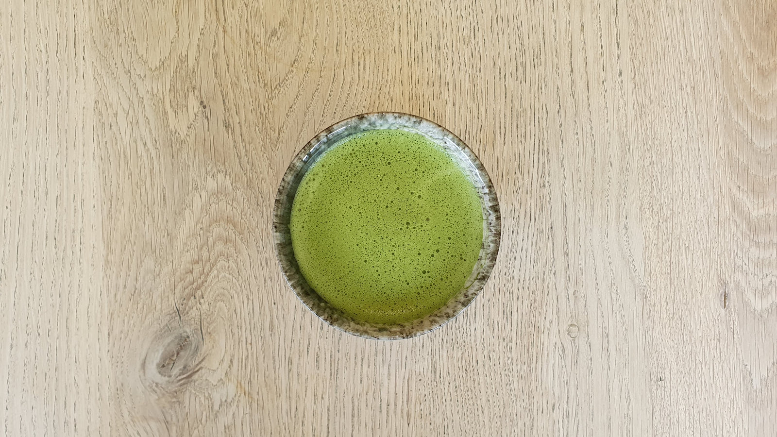 Ceremonial matcha green tea brew that's been whisked in a cup centred on a wooden background