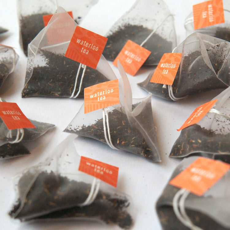 A handful of compostable English Breakfast tea bags laid out on a white surface displaying the tag 'Waterloo Tea'