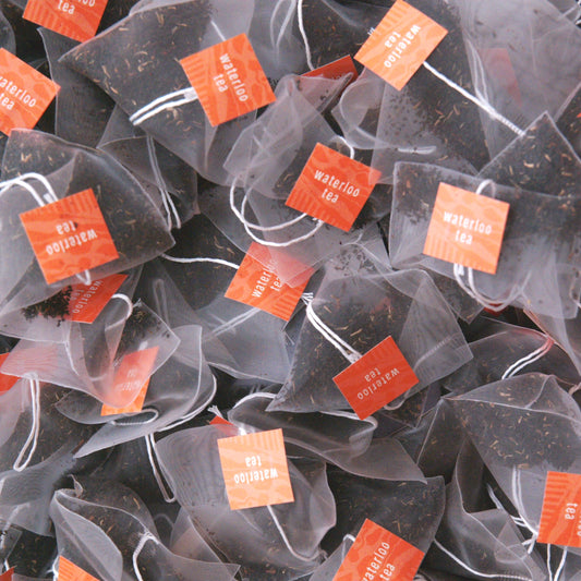 A pile of English Breakfast Tea bags showing a high quality Sri Lankan breakfast tea. The bags are compostable, with a white string and orange tag that reads 'Waterloo Tea'