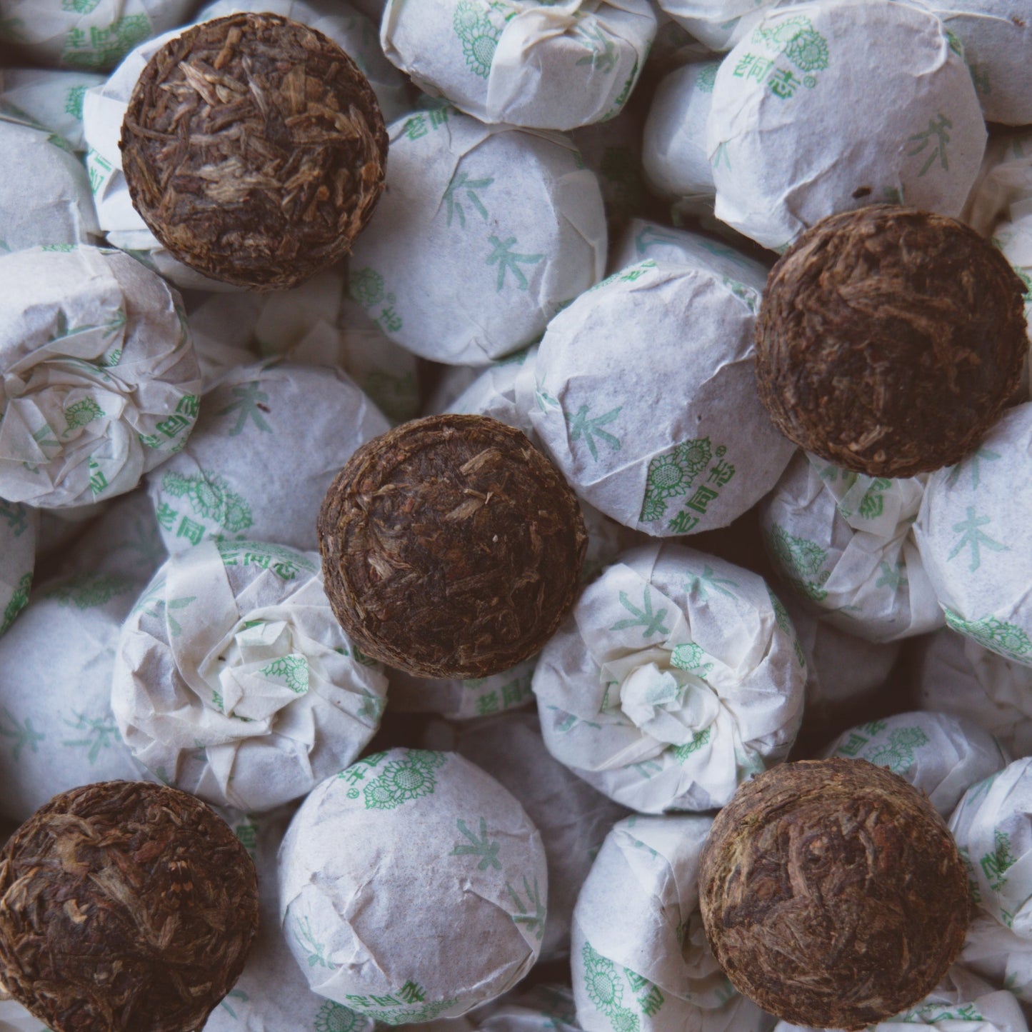 Close up of a pile of Haiwan raw puerh tea mini cakes. A handful on the top are unwrapped showing the brown mini tuo cakes and their pressed form. 