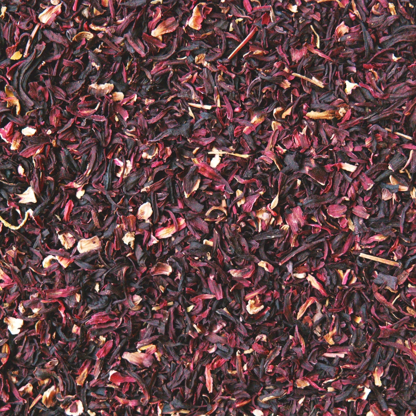 A close up view of herbal loose leaf tea. The image is specifically of dried cut hibiscus flower. It's showing it dark and bright red tones. 