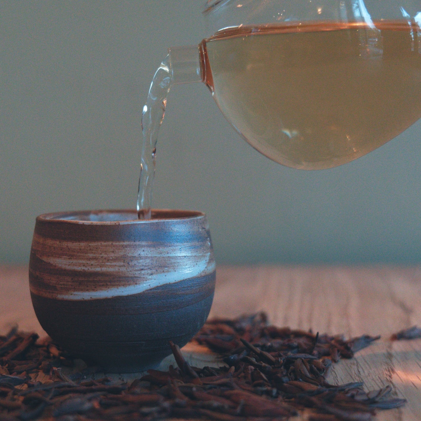 Wild purple raw puerh tea being poured into a small cup with loose leaf tea on the table surrounding it. 