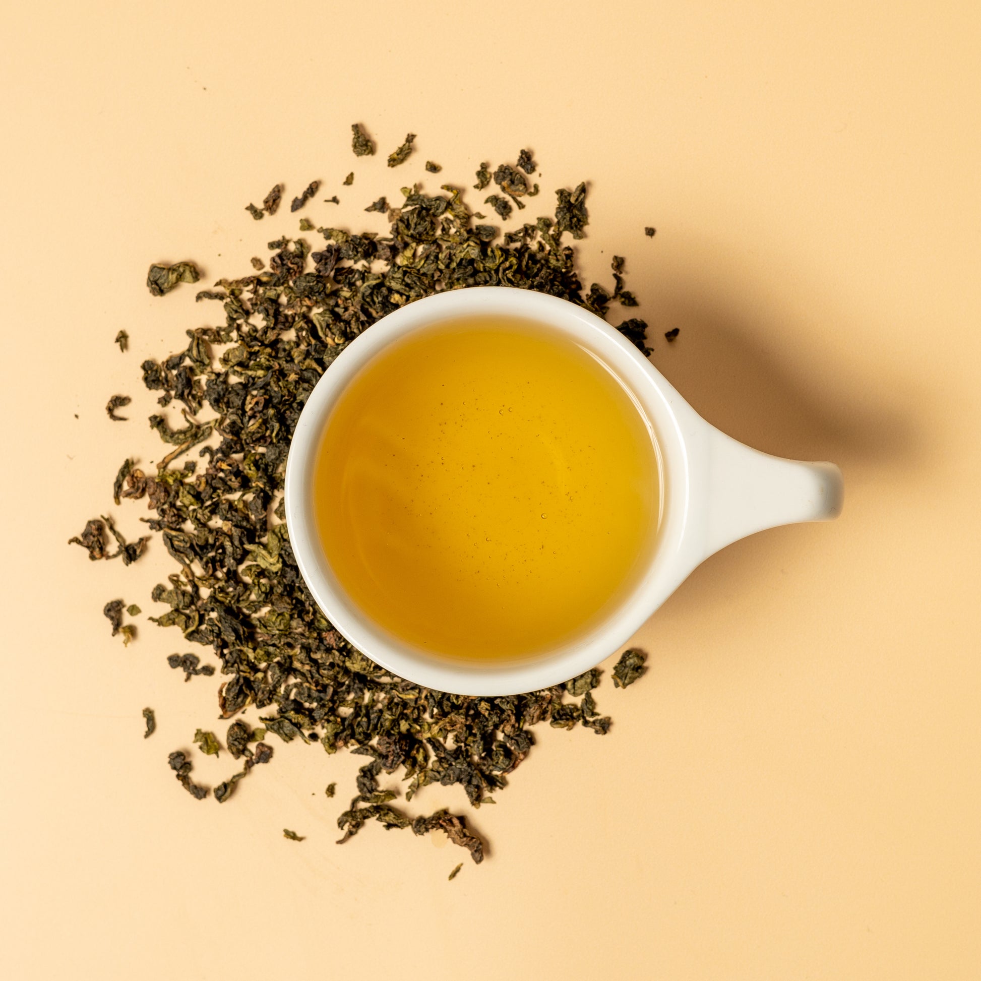 Brewed cup of Iron Goddess of Mercy loose leaf oolong tea surround by tea leaves from Anxi, China. 